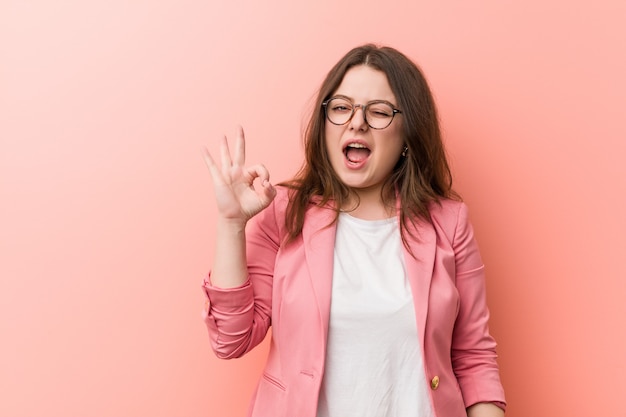 Jeune femme caucasienne de taille plus entreprise clin d'oeil un œil et est titulaire d'un geste correct avec la main. Photo Premium