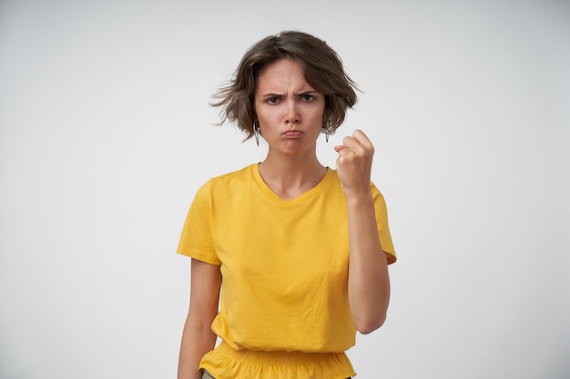 Jeune Femme En Colere Avec Une Coupe De Cheveux Courte Menace Avec Le Poing Leve Tout En Regardant De Travers Portant Des Vetements Decontractes En Position Debout Photo Gratuite