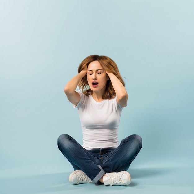 Jeune femme paresseuse avec ses deux mains dans les cheveux sur fond bleu Photo gratuit