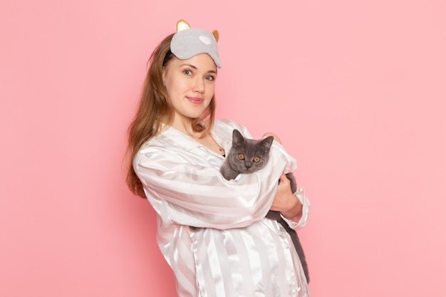 Jeune Femme En Pyjama Et Masque De Sommeil Posant Avec Sourire Et Chaton Gris Sur Rose Photo Gratuite