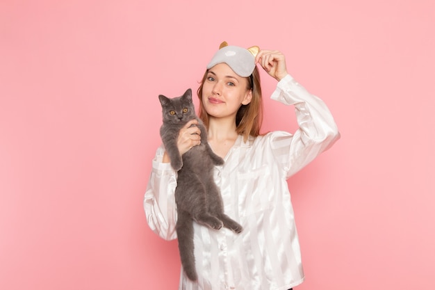 Jeune Femme En Pyjama Et Masque De Sommeil Posant Avec Sourire Et Mignon Chaton Gris Sur Rose Photo Gratuite