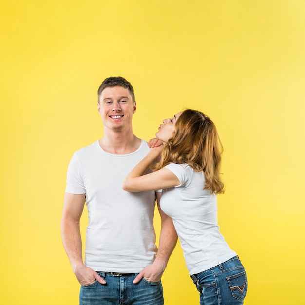 Jeune femme se penchant sur l'épaule de son petit ami soufflant un baiser sur fond jaune Photo gratuit