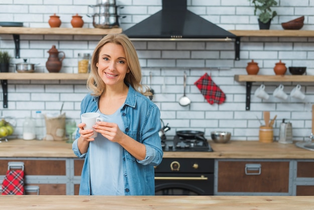 Jeune Femme Tenant Tasse De Café à La Main Debout Dans La Cuisine Photo Gratuite 8491