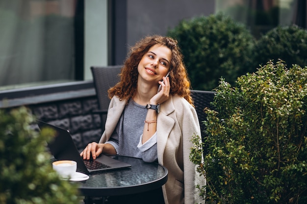 Jeune femme travaillant sur un ordinateur devant le café Photo gratuit