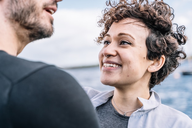 Jeune fille aux cheveux bouclés et nez percé regardant sa partenaire avec la mer floue dans le Photo gratuit