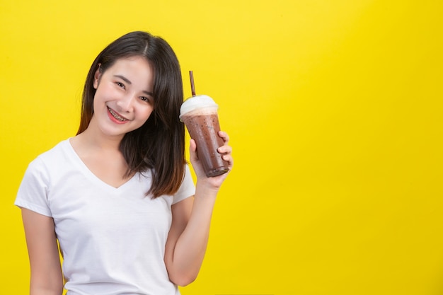 La jeune fille boit de l'eau froide dans du cacao dans un verre en plastique transparent sur un fond jaune. Photo gratuit