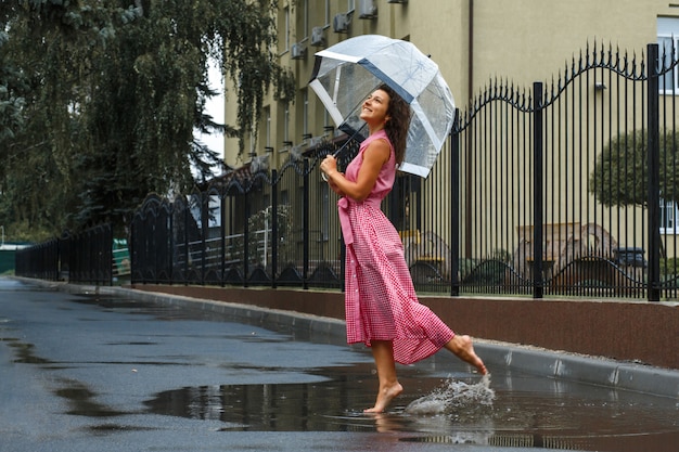 Jeune, fille, dans, a, robe rouge, à, a, parapluie transparent, danser sous la pluie, tenir dans, a, flaque eau Photo Premium