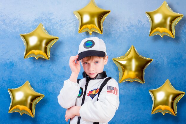 Jeune garçon garçon jouant dans un astronaute en costume d'astronaute blanc et rêvant de voler dans le cosmos à travers les étoiles en restant à proximité des ballons de l'étoile d'or Photo Premium
