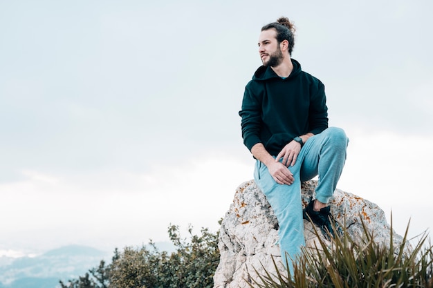Jeune homme assis au sommet d'un rocher en regardant la vue Photo gratuit