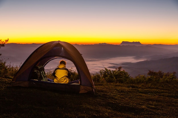 Un jeune homme assis dans la tente avec regardant le paysage de montagne en hiver Photo gratuit