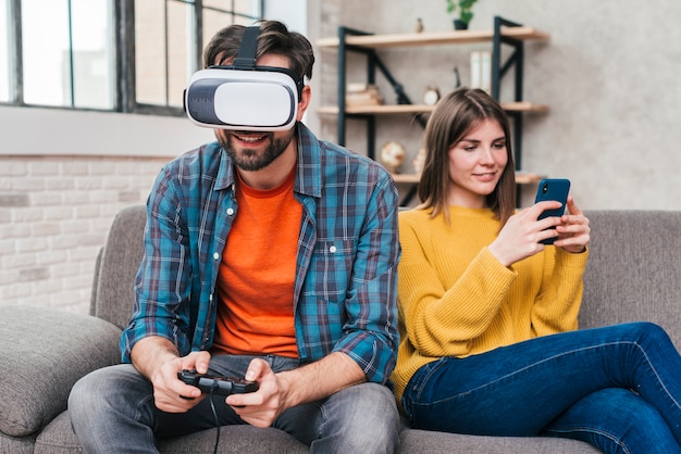 Jeune homme portant des lunettes de réalité virtuelle jouant au jeu vidéo avec sa femme à l'aide de téléphone portable Photo gratuit