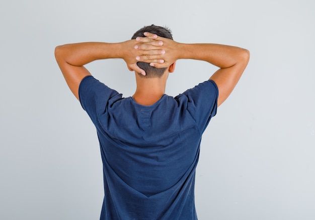 Jeune Homme En T Shirt Bleu Foncé Croisant Les Mains Derrière La Tête Et à La Vue Détendue 