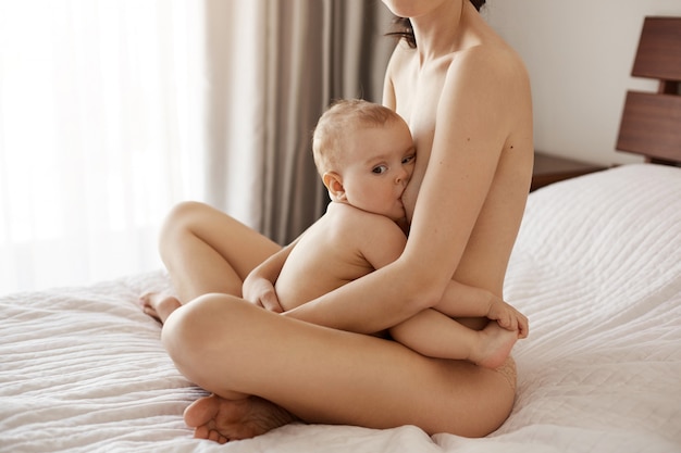 Jeune Maman Nue Attrayante Allaitant Son Bebe Nouveau Ne En Souriant Assis Sur Le Lit A La Maison Photo Gratuite