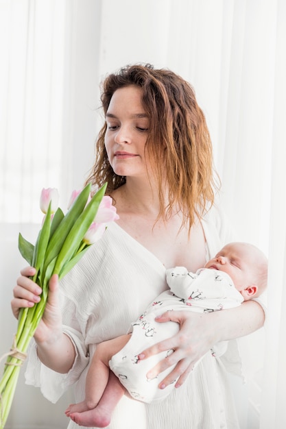 Jeune Maman Portant Son Bebe Avec Des Fleurs De Tulipes Roses Photo Gratuite