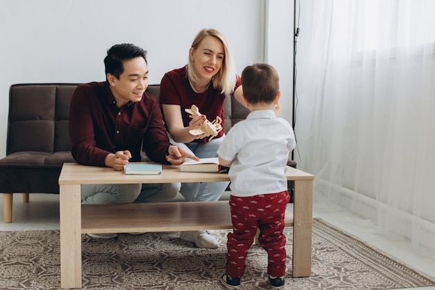 Jeune Papa Asiatique Et Maman Blonde Europeenne Jouent Assis Avec Son Fils Dans Une Salle Lumineuse Photo Premium