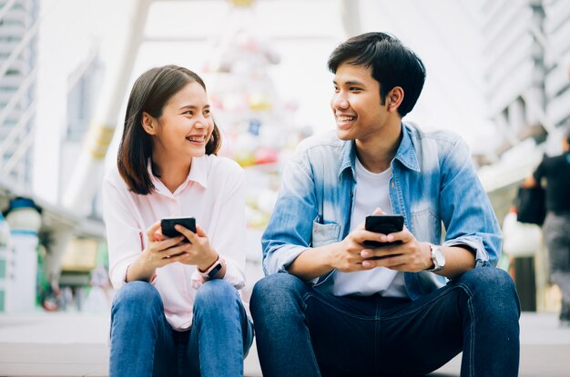 Les jeunes utilisent un smartphone et sourient lorsqu'ils sont assis sur leur temps libre. Photo Premium