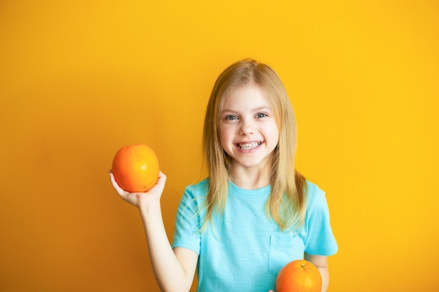 Joli Bebe De 8 Ans Sur Un Mur Orange Jolie Fille Blonde Avec Des Appelsins Dans Ses Mains Sourit Photo Premium