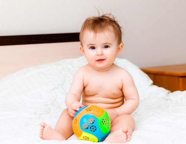 Joli Bebe Blond Jouant Avec Un Ballon Assis Sur Le Lit Dans La Chambre Heureux Bebe De 6 Mois Jouant Avec Un Ballon Photo Premium