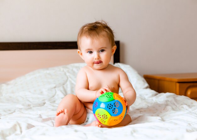 Joli Bebe Blond Jouant Avec Un Ballon Assis Sur Le Lit Dans La Chambre Heureux Bebe De 6 Mois Jouant Avec Un Ballon Photo Premium