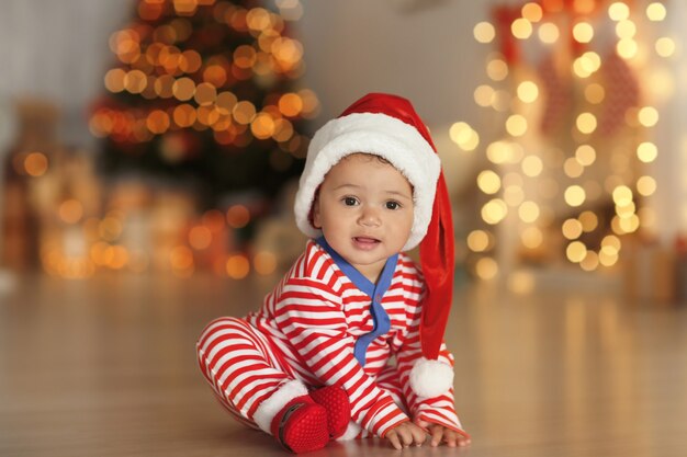 Joli Petit Bebe Avec Un Bonnet De Noel Au Sol Et Des Lumieres De Noel Floues A La Surface Photo Premium