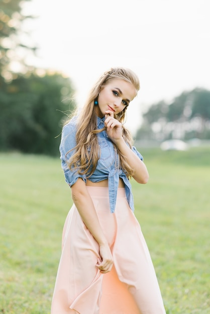 Jolie belle fille douce dans une chemise en jean et jupe en mousseline de soie rose sourit mystérieusement Photo Premium