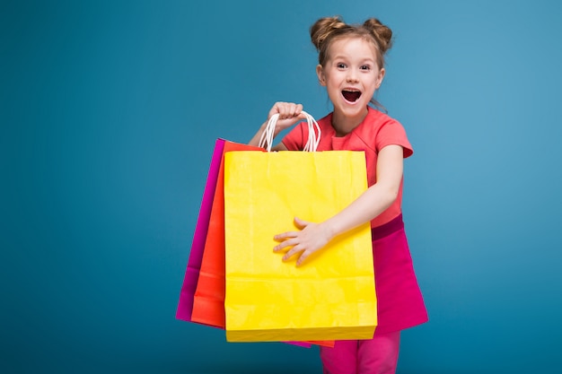 Jolie petite fille mignonne en robe rose est titulaire d'un sac en papier violet Photo Premium