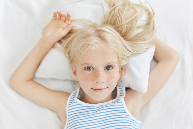 Jolie Petite Fille Reposant Sur Un Lit Blanc Regardant Avec Des Yeux Bleus Fille Blonde Aux Yeux Bleus De Reve Dans Une Chambre Confortable Photo Gratuite