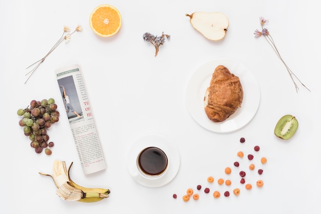 Journal roulé avec tasse à café; croissant et fruits sur fond blanc Photo gratuit