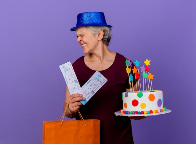 Joyeuse Femme Agee Portant Chapeau De Fete Detient Des Billets D Avion Sac A Provisions Papier Et Gateau D Anniversaire A Cote Isole Sur Mur Violet Avec Espace Copie Photo Gratuite