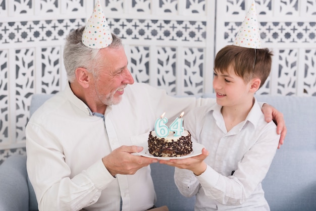 Joyeux Grand Pere Et Petit Fils Se Regardant Tout En Tenant Un Delicieux Gateau Avec Une Bougie Photo Gratuite