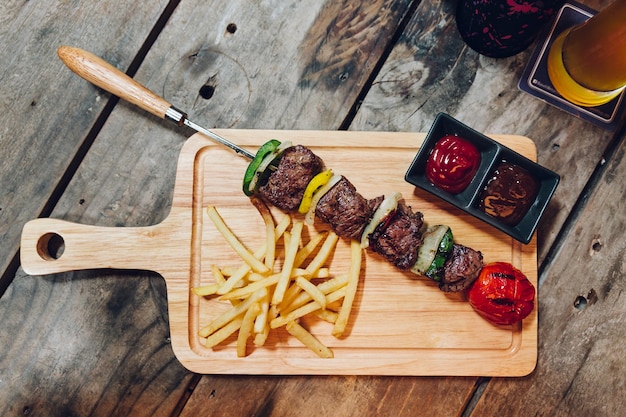 Kebab de boeuf bbq servi avec frites, sauce tomate et sauce barbecue sur une assiette en bois. Photo Premium