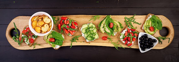 Lay plat de table de dîner végétarien sain. sandwichs à la tomate, concombre, avocat, fraise, fines herbes et olives, snacks. bannière. propre manger, nourriture végétalienne Photo Premium