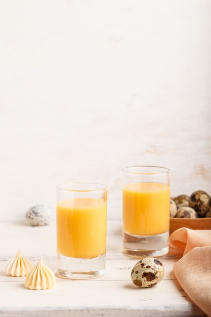Liqueur D'oeuf Doux En Verre Avec Des Oeufs De Caille Et Des Meringues Sur Bois Blanc. Vue Latérale, Espace Copie, Vertical. Photo Premium