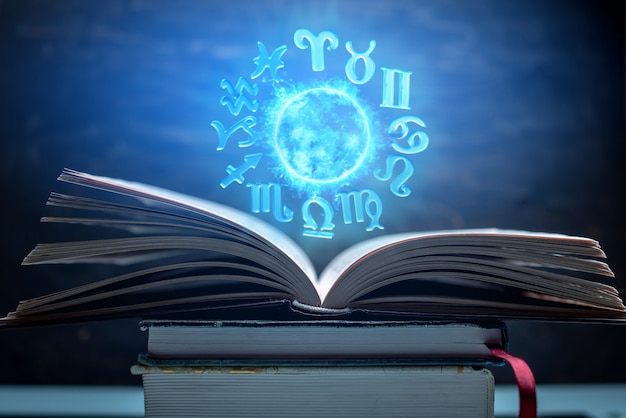 Livre ouvert sur l'astrologie. le globe magique rougeoyant avec des signes du zodiaque à la lumière bleue Photo Premium