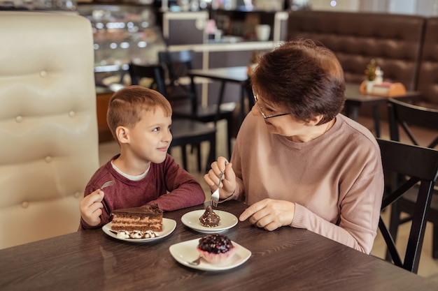 Loisirs Et Divertissements En Famille Grand Mere Heureuse Avec Des Cheveux Courts Des Lunettes Et Un Petit Fils Se Reposent Dans Un Cafe Ils Mangent Des Gateaux Avec Des Laits Frappes Photo Premium