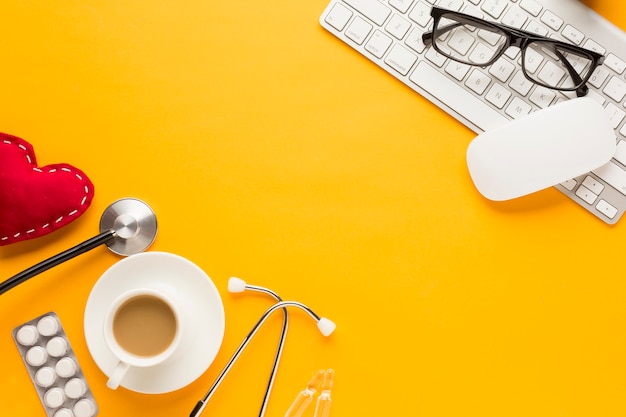 Lunettes de vue sur souris sans fil et clavier avec stéthoscope; cœur cousu; comprimé et tasse à café emballés sous blister contre une surface jaune Photo gratuit