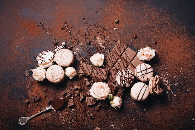 Macarons; roses roses; sirop et barre de chocolat saupoudrés de café en poudre sur fond noir Photo gratuit