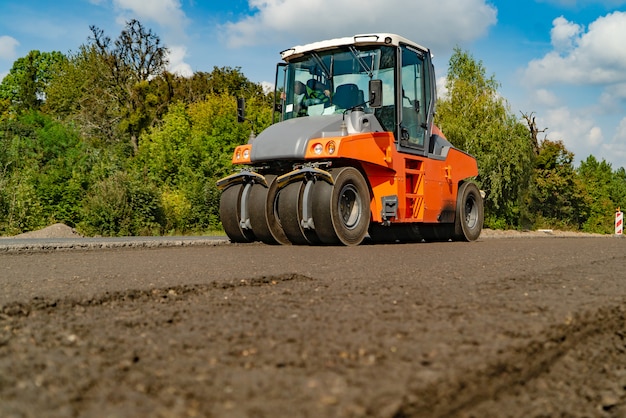 Les machines de construction pour les travaux routiers traversent un nouvel asphalte en été des arbres Photo Premium