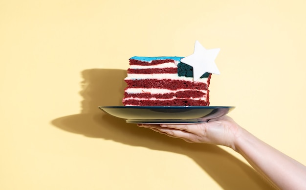 Main Feminine Tenant Une Assiette Avec Un Morceau De Gateau Sous La Forme Du Drapeau Des Etats Unis Sur Fond Jaune Celebrant Le Jour De L Independance En Gros Plan Photo Premium