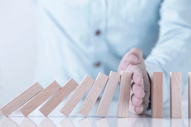 Main d'homme d'affaires stoppant l'effet domino pour la gestion et la solution, stratégie de concept et intervention réussie Photo Premium