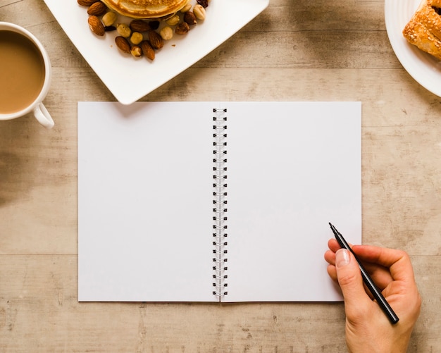 Main qui écrit sur un cahier avec café Photo gratuit