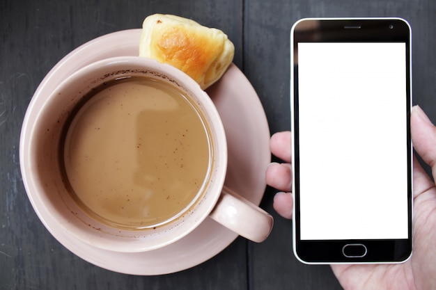 Main tenant le smartphone avec une tasse de café brune sur une table en bois noire Photo Premium