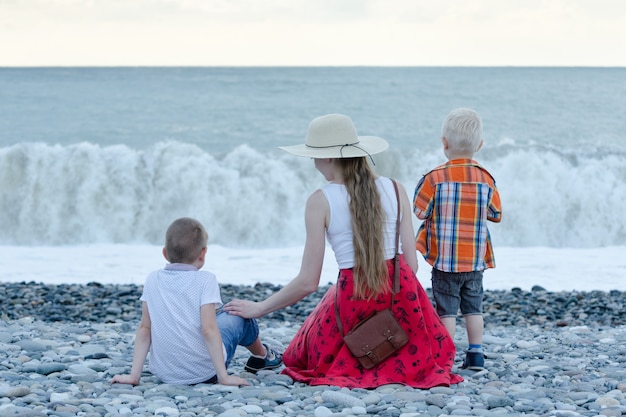 Maman Et Deux Fils Assis Sur La Plage Et Regardant Les Vagues. Vue Arrière Photo Premium