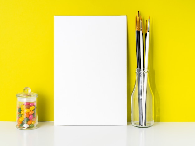 Maquette en toile blanche, bonbons dans un bocal, pinceaux sur fond jaune vif. concept Photo Premium