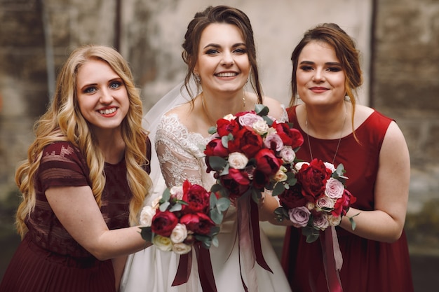 La mariée et les demoiselles d'honneur en robes rouges posent à l'extérieur sur la vieille rue humide Photo gratuit