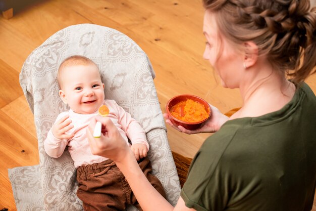 Mere Nourrit Un Bebe Qui Rit Avec De La Puree De Legumes A Partir D Une Cuillere En Plastique A La Maison Photo Premium