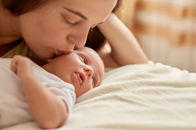 Mere Et Son Bebe Nouveau Ne Ensemble Allonge Sur Le Lit Sur Une Couverture Heureuse Mere Embrassant Et Etreignant Bebe Enfant Regardant Ailleurs Et Etudiant Les Choses Exterieures Maternite Et Parentalite Photo