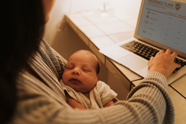 Mère utilisant un ordinateur et tenant son bébé Photo Premium