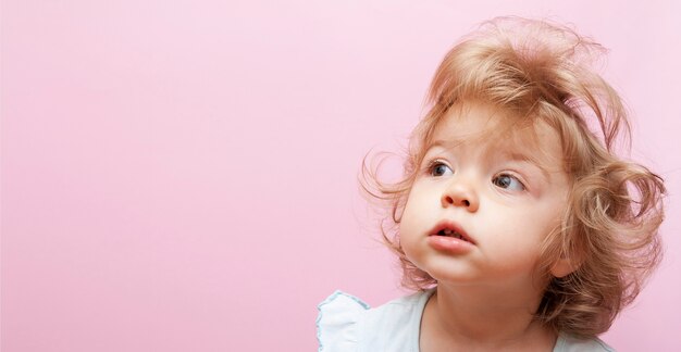 Mignon Enfant Surpris En Detournant Les Yeux Avec Des Cheveux Boucles Et Une Coiffure Moelleuse Sur Fond Rose Photo Premium