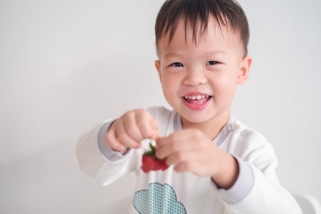 Mignon Heureux Souriant Petit Asiatique 2 3 Ans Bebe Enfant Garcon A L Aide Des Mains Manger Des Fraises Des Collations Saines Et Le Concept D Auto Alimentation Photo Premium